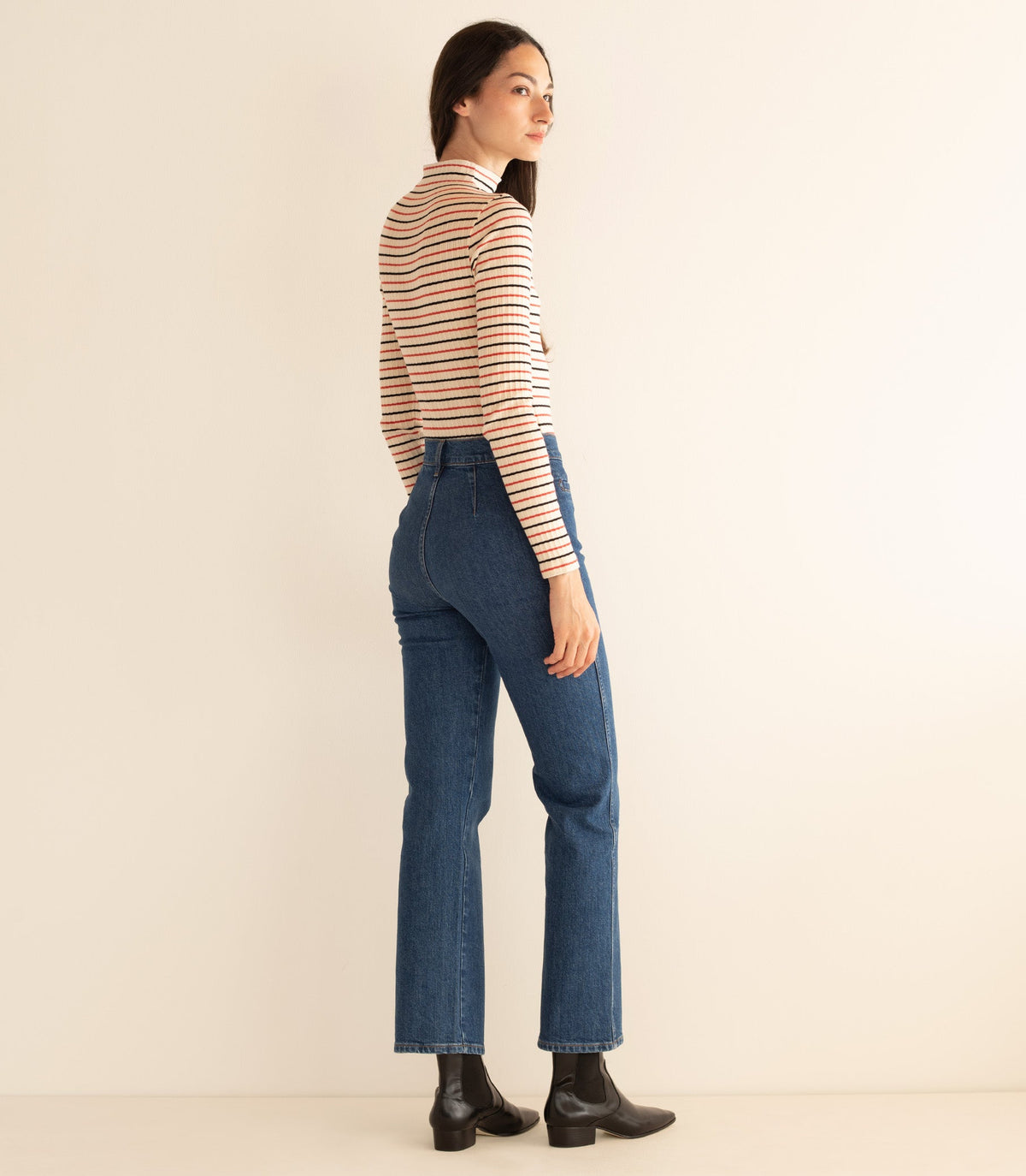 Woman wearing a striped long-sleeve top and blue jeans against a beige background