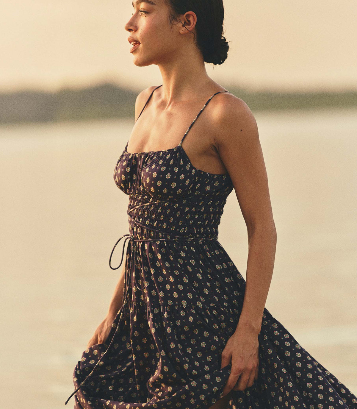 Woman in a navy foulard dress standing on a beach at sunset.