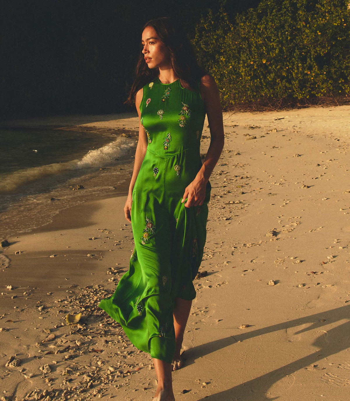 Woman in a green dress walking on a beach at sunset