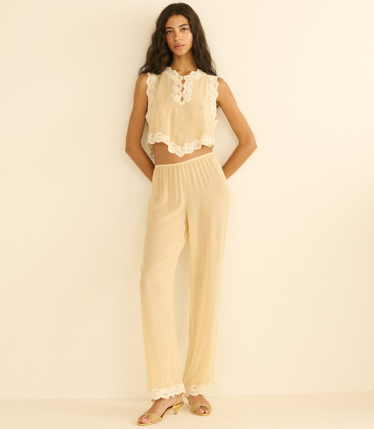 Woman wearing a beige sleeveless top and pants against a beige background