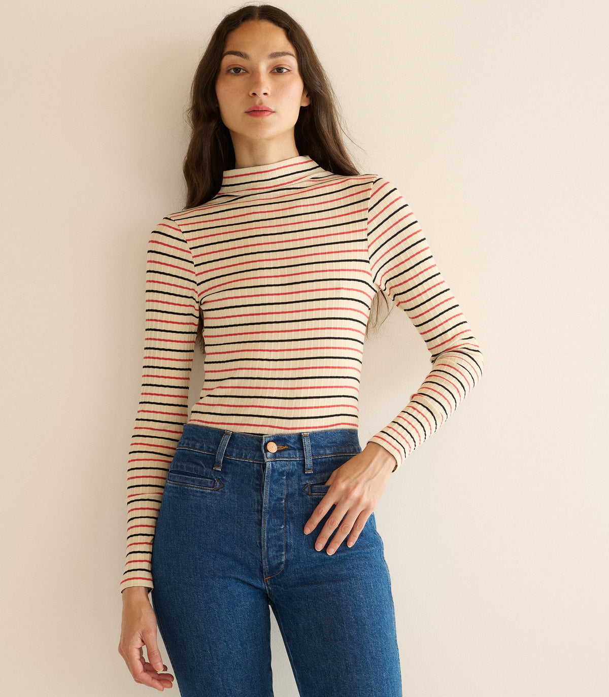 Woman wearing a striped long-sleeve top and blue jeans against a beige background