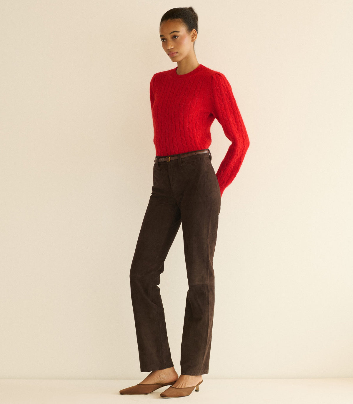 Person wearing a red sweater and brown pants on a beige background
